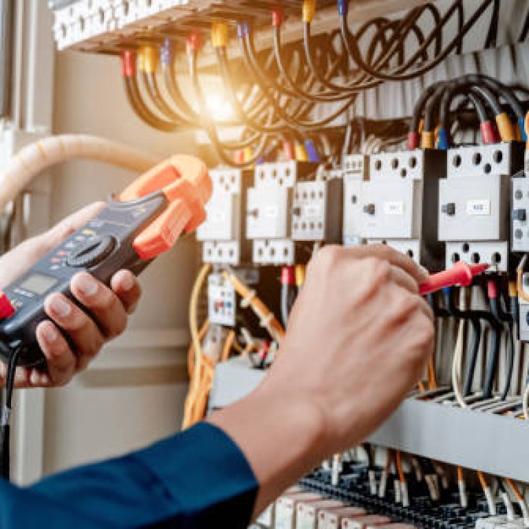 Electrician engineer uses a multimeter to test the electrical installation and power line current in an electrical system control cabinet.
